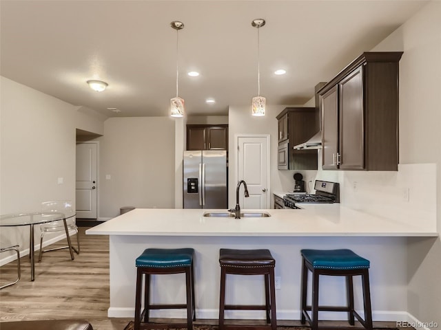 kitchen with sink, a kitchen bar, light hardwood / wood-style floors, stainless steel appliances, and decorative light fixtures