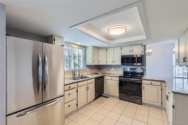 kitchen with light tile patterned floors, a sink, a tray ceiling, black appliances, and light stone counters
