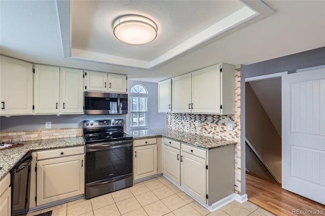 kitchen featuring a tray ceiling, electric range, tasteful backsplash, black dishwasher, and stainless steel microwave