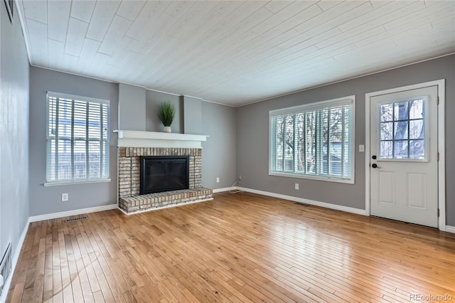 unfurnished living room with a healthy amount of sunlight, wood-type flooring, visible vents, and a brick fireplace