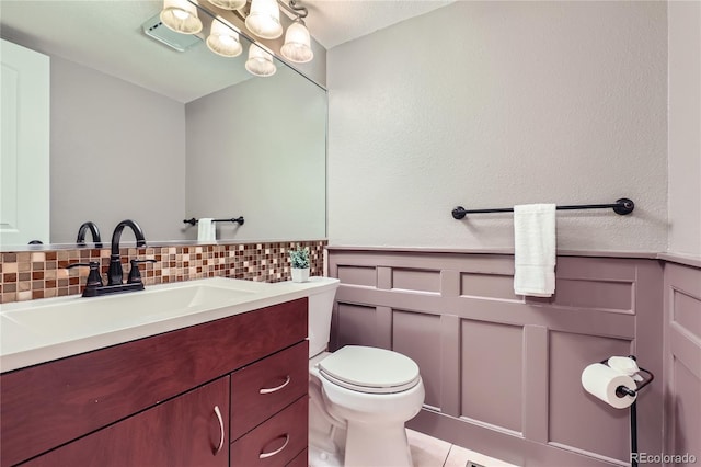 half bathroom featuring toilet, vanity, and a wainscoted wall