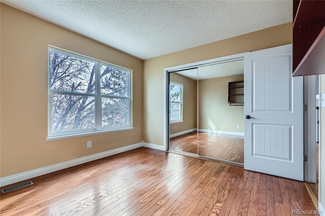unfurnished bedroom featuring a textured ceiling, a closet, visible vents, wood-type flooring, and baseboards