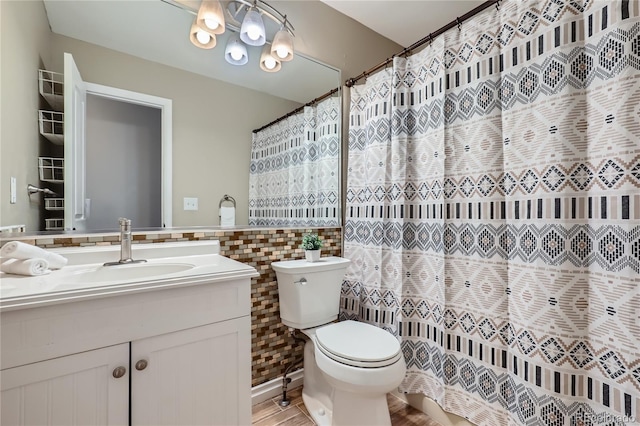full bathroom with a notable chandelier, toilet, tile walls, vanity, and a wainscoted wall