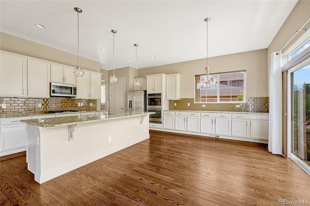 kitchen with dark wood-type flooring, stainless steel appliances, tasteful backsplash, and a center island with sink