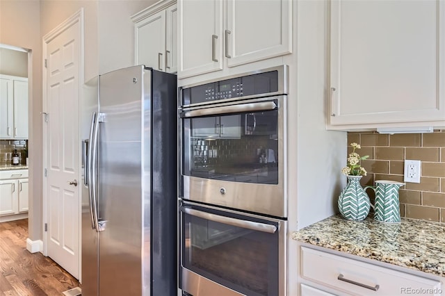 kitchen with appliances with stainless steel finishes, light stone counters, wood finished floors, white cabinetry, and backsplash