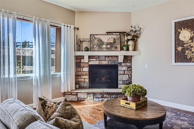 living room featuring a stone fireplace, baseboards, and wood finished floors