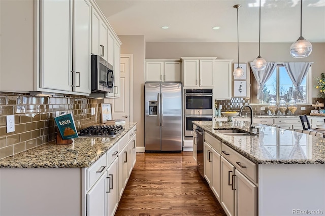 kitchen with white cabinets, dark wood-style flooring, a sink, stainless steel appliances, and backsplash