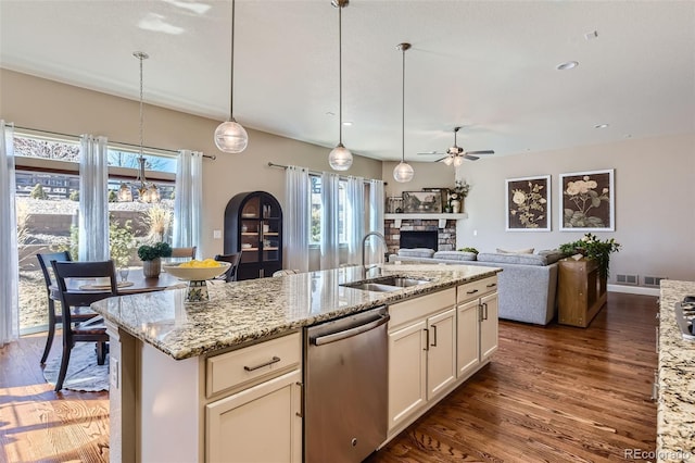 kitchen with light stone counters, dark wood-type flooring, a sink, a stone fireplace, and stainless steel dishwasher