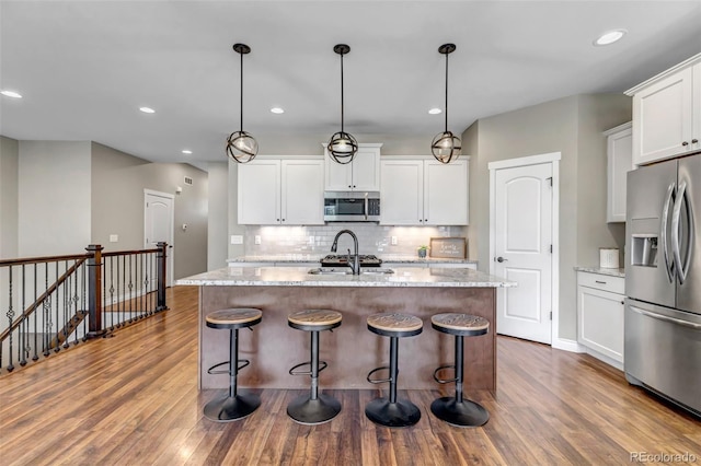 kitchen featuring white cabinets, an island with sink, stainless steel appliances, decorative backsplash, and wood finished floors