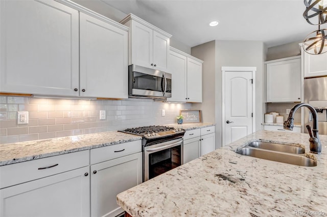 kitchen featuring light stone counters, a sink, stainless steel appliances, white cabinetry, and backsplash