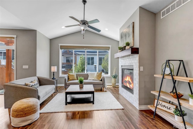 living room with a glass covered fireplace, a ceiling fan, wood finished floors, and visible vents