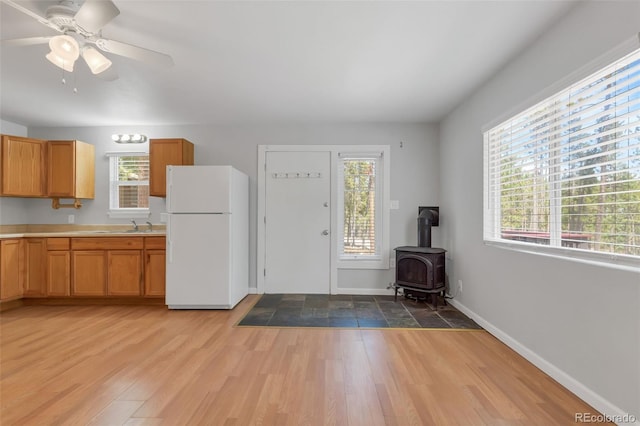 kitchen with a wood stove, sink, white fridge, ceiling fan, and light hardwood / wood-style floors