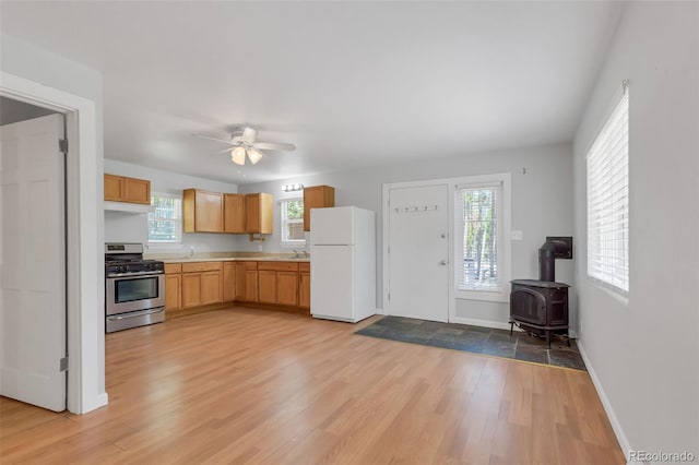 kitchen with a wood stove, sink, white fridge, stainless steel gas range, and light hardwood / wood-style flooring