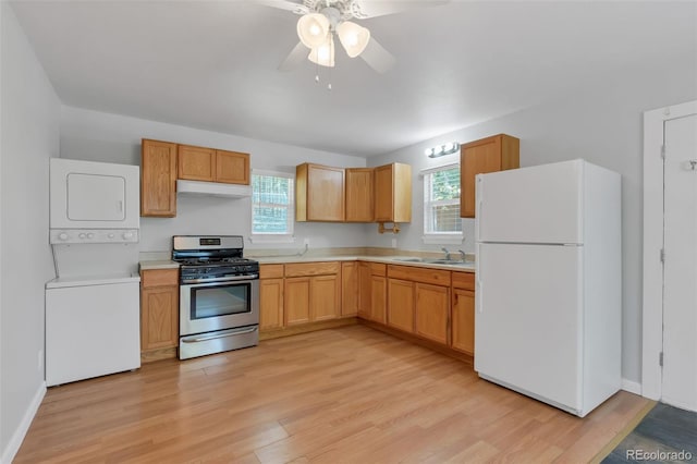 kitchen featuring stacked washer and dryer, sink, light hardwood / wood-style flooring, stainless steel range with gas cooktop, and white fridge