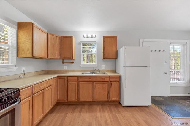 kitchen featuring sink, stainless steel stove, light hardwood / wood-style flooring, and white fridge