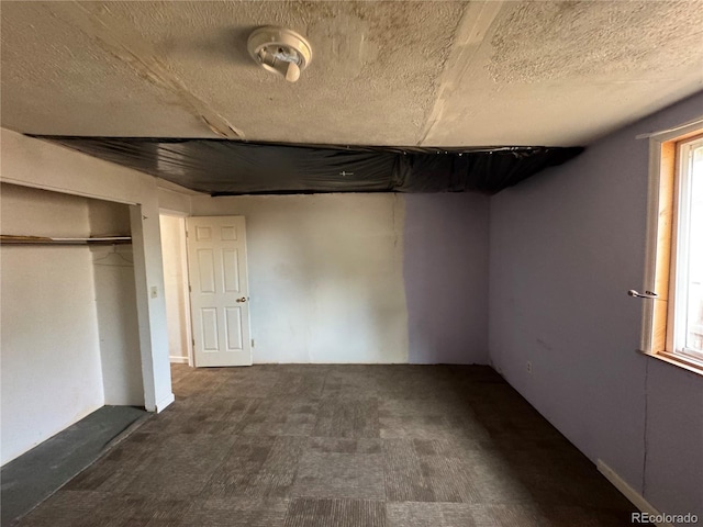 unfurnished bedroom featuring a closet, a textured ceiling, multiple windows, and dark carpet