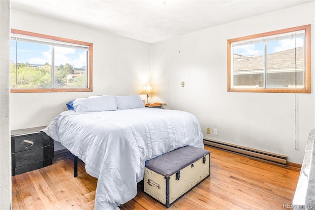 bedroom featuring a baseboard heating unit, light wood-style floors, and multiple windows