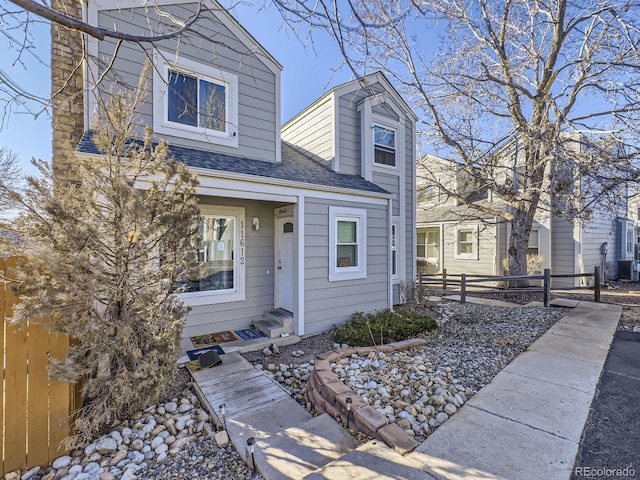 view of front of home with entry steps, roof with shingles, fence, and central AC unit