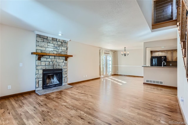 unfurnished living room with a stone fireplace, light hardwood / wood-style flooring, a textured ceiling, and a chandelier