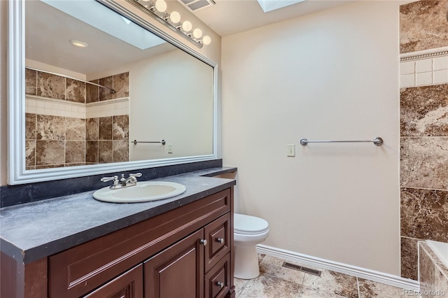 bathroom featuring vanity, toilet, a skylight, and a tile shower