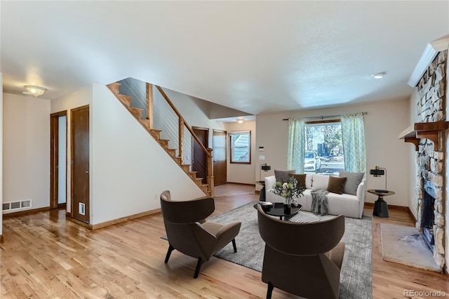 living room featuring light wood finished floors, stairway, a fireplace, and visible vents