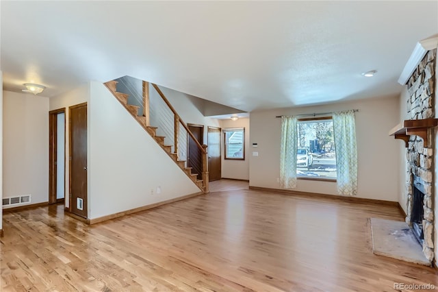 unfurnished living room featuring a stone fireplace, visible vents, baseboards, stairway, and light wood-type flooring