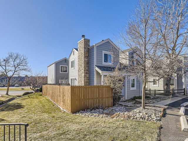 view of side of home with fence, a chimney, and a lawn