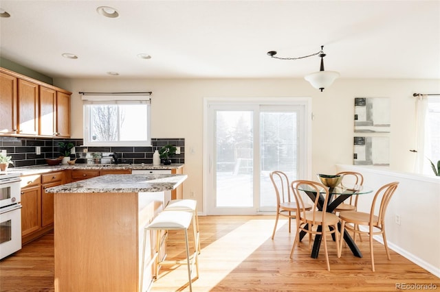 kitchen with a center island, hanging light fixtures, light stone countertops, tasteful backsplash, and light hardwood / wood-style floors