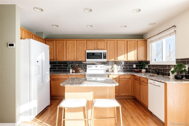 kitchen featuring a center island, white appliances, sink, light hardwood / wood-style flooring, and light stone countertops