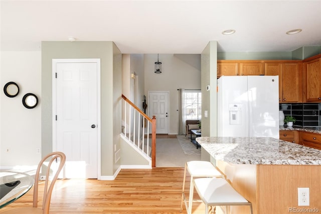 kitchen featuring backsplash, white fridge with ice dispenser, a kitchen island, light stone counters, and a breakfast bar area