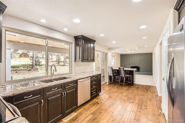 12454 Antelope Trl, Parker, CO 80138 - kitchen with appliances with stainless steel finishes, a brick fireplace, light wood-style floors, light stone counters, and recessed lighting