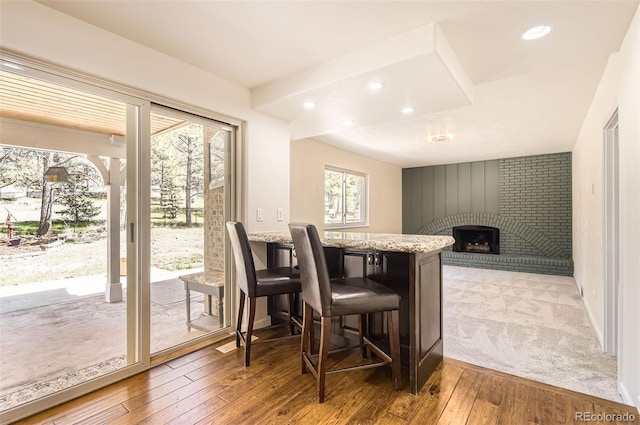 12454 Antelope Trl, Parker, CO 80138 - kitchen with a brick fireplace, light stone countertops, light wood-type flooring, recessed lighting, and a breakfast bar