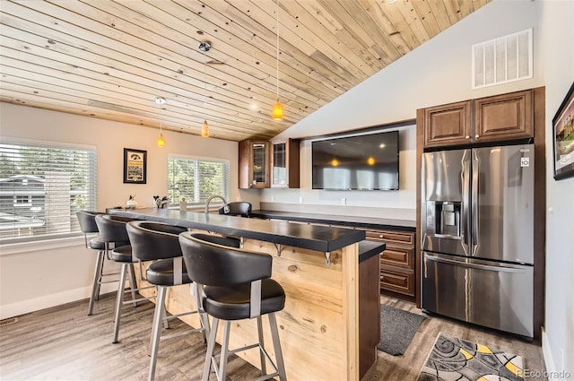 12454 Antelope Trl, Parker, CO 80138 - kitchen with stainless steel refrigerator with ice dispenser, a kitchen breakfast bar, vaulted ceiling, dark countertops, and wood finished floors