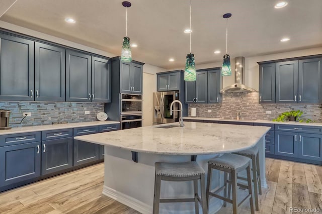 kitchen featuring a center island with sink, hanging light fixtures, light hardwood / wood-style floors, and wall chimney range hood