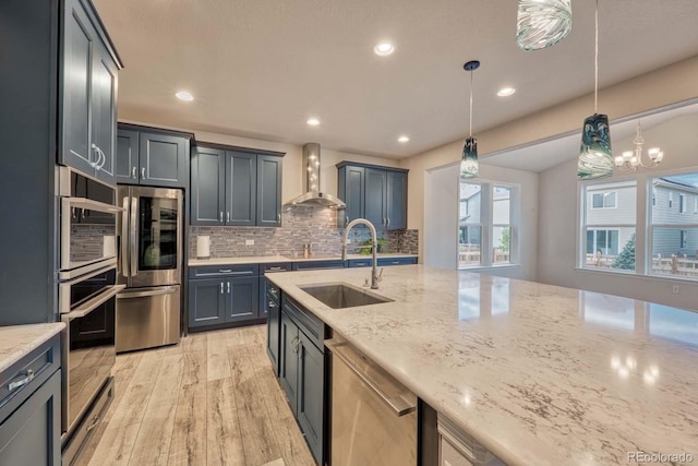 kitchen featuring pendant lighting, light wood-type flooring, sink, wall chimney range hood, and stainless steel appliances