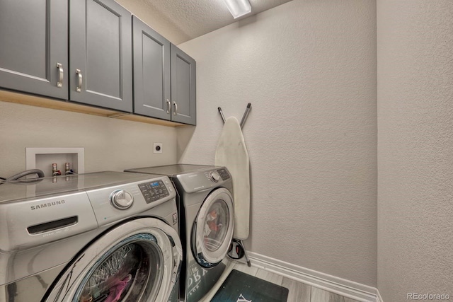 laundry room featuring cabinets, light hardwood / wood-style floors, a textured ceiling, and washing machine and dryer