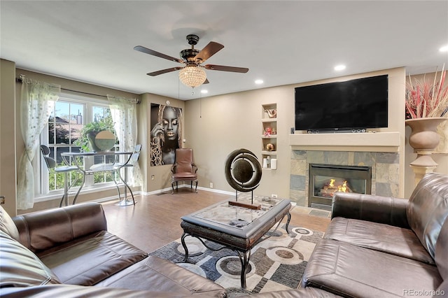 living room with ceiling fan, light wood-type flooring, a fireplace, and built in features