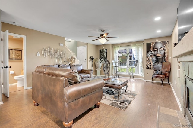 living room featuring light wood-type flooring, a tiled fireplace, and ceiling fan