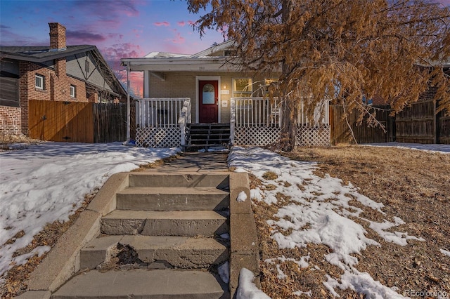 view of front of house with covered porch, brick siding, and fence