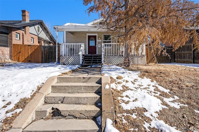 bungalow-style house with a porch, fence, and brick siding