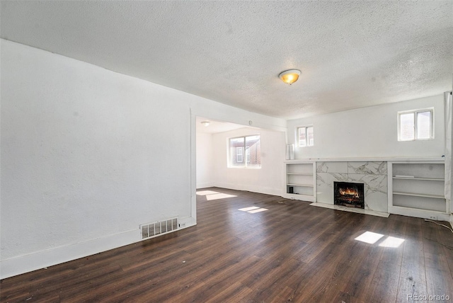 unfurnished living room with dark wood-style floors, a high end fireplace, a healthy amount of sunlight, and visible vents