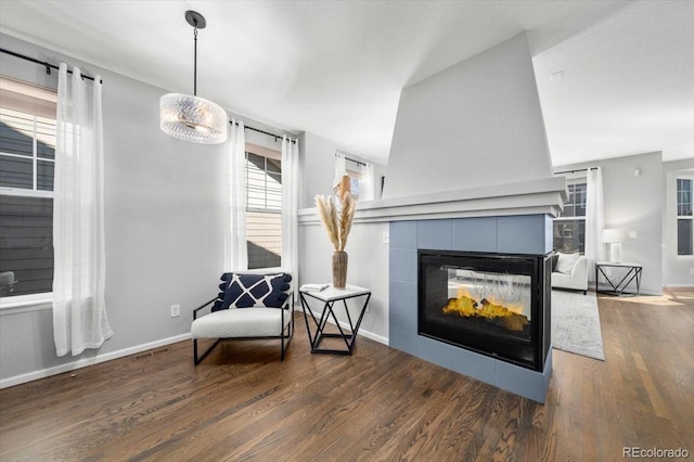 living area with a tiled fireplace, wood finished floors, visible vents, and baseboards