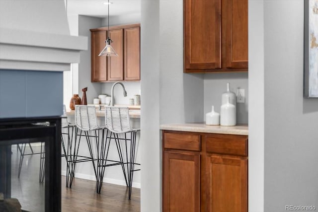 kitchen featuring brown cabinets, dark wood-style flooring, hanging light fixtures, light countertops, and a sink