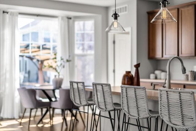 kitchen with hanging light fixtures, a kitchen bar, visible vents, and brown cabinets