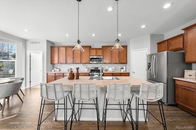 kitchen with dark wood-type flooring, visible vents, appliances with stainless steel finishes, brown cabinets, and a kitchen bar