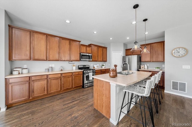 kitchen with brown cabinets, a breakfast bar area, visible vents, appliances with stainless steel finishes, and dark wood-type flooring