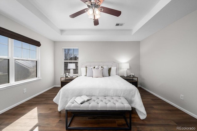 bedroom with baseboards, visible vents, ceiling fan, wood finished floors, and a tray ceiling