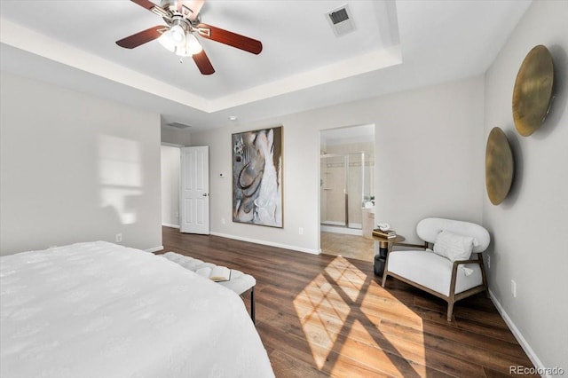 bedroom with a tray ceiling, wood finished floors, visible vents, and baseboards