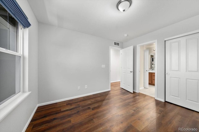 unfurnished bedroom with baseboards, visible vents, dark wood finished floors, and a closet