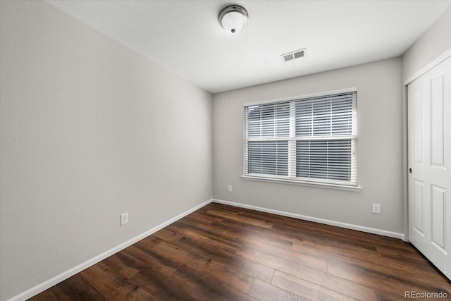 spare room with dark wood-style flooring, visible vents, and baseboards